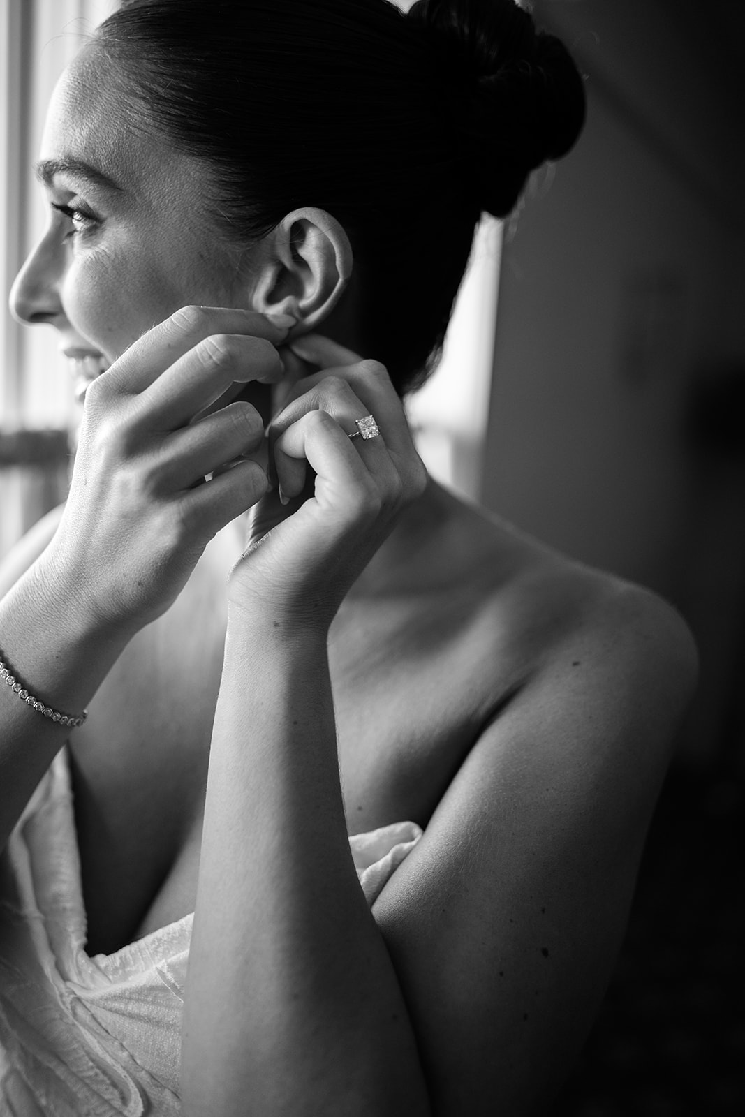 Black and white film photo of the bride smiling softly while putting on her earrings.